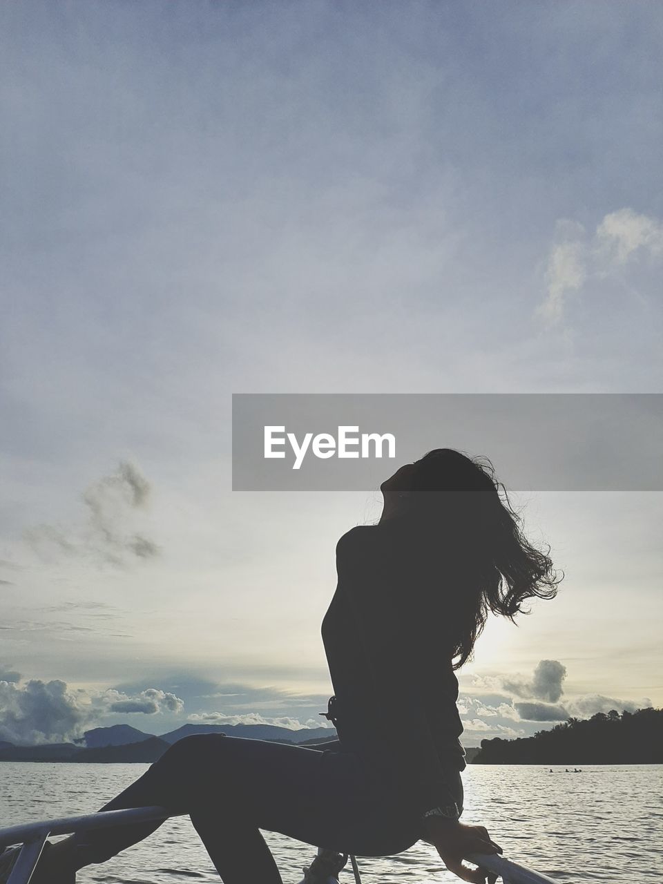 Woman sitting on shore against sky during sunset