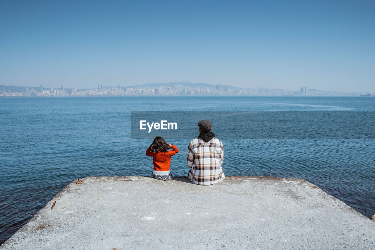 rear view of woman sitting at beach against clear sky