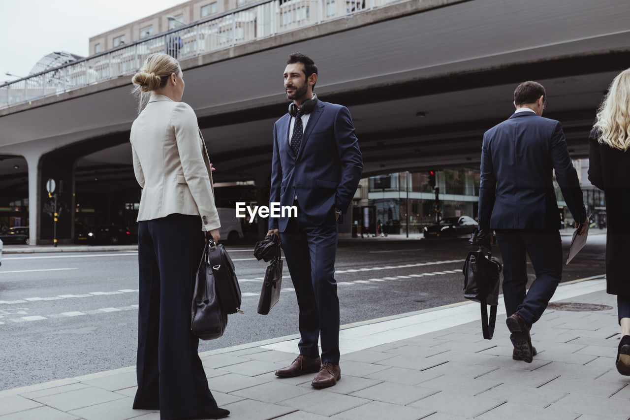 Entrepreneur with bag talking to female coworker while standing in city