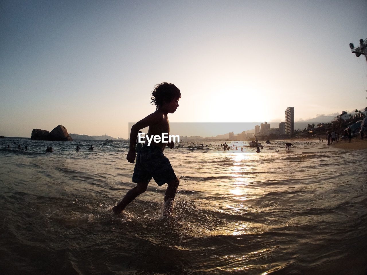 Side view of shirtless boy playing in sea against clear sky