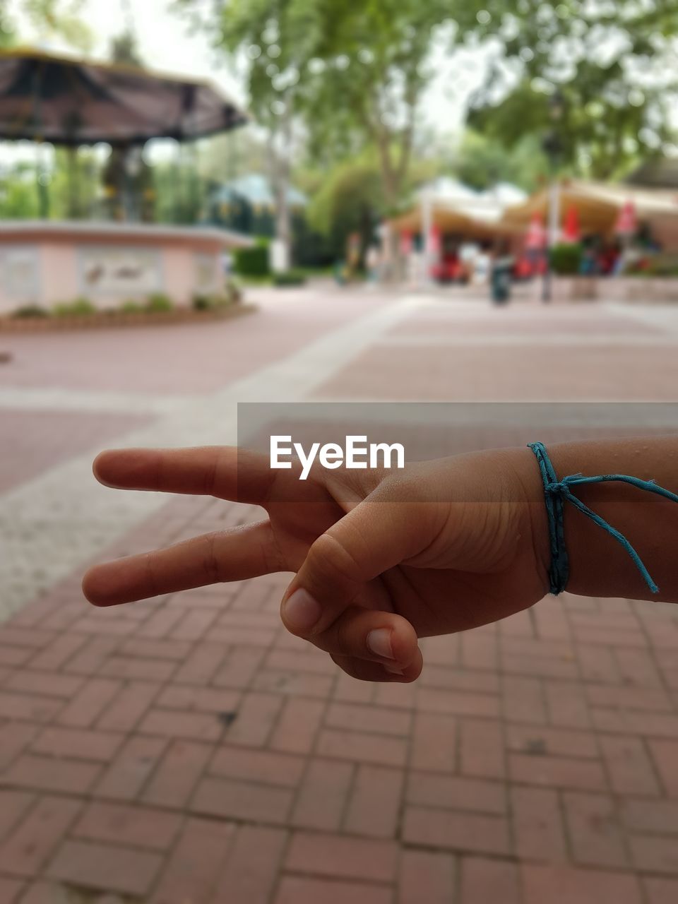 Cropped hand of child gesturing peace sign over footpath at park