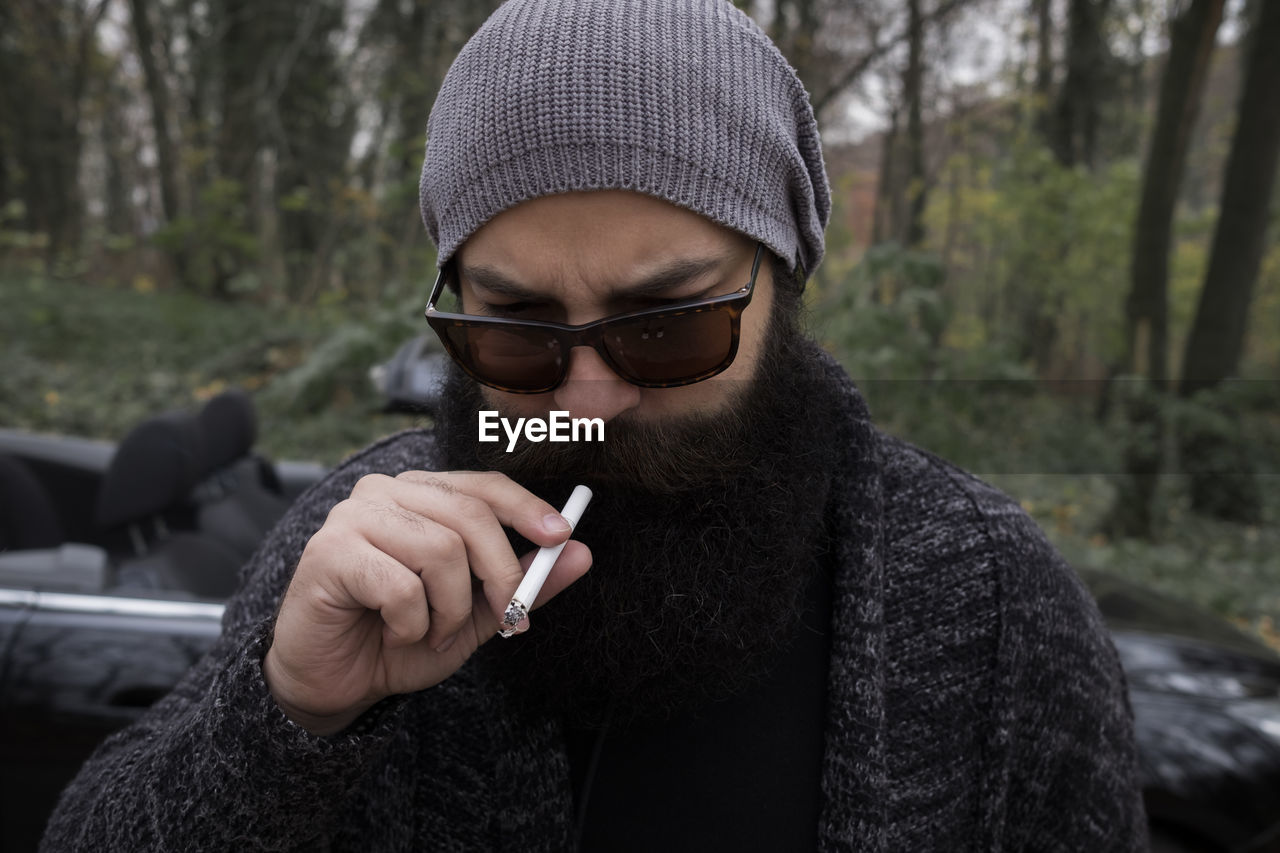 Man wearing knit hat smoking cigarette while standing in forest