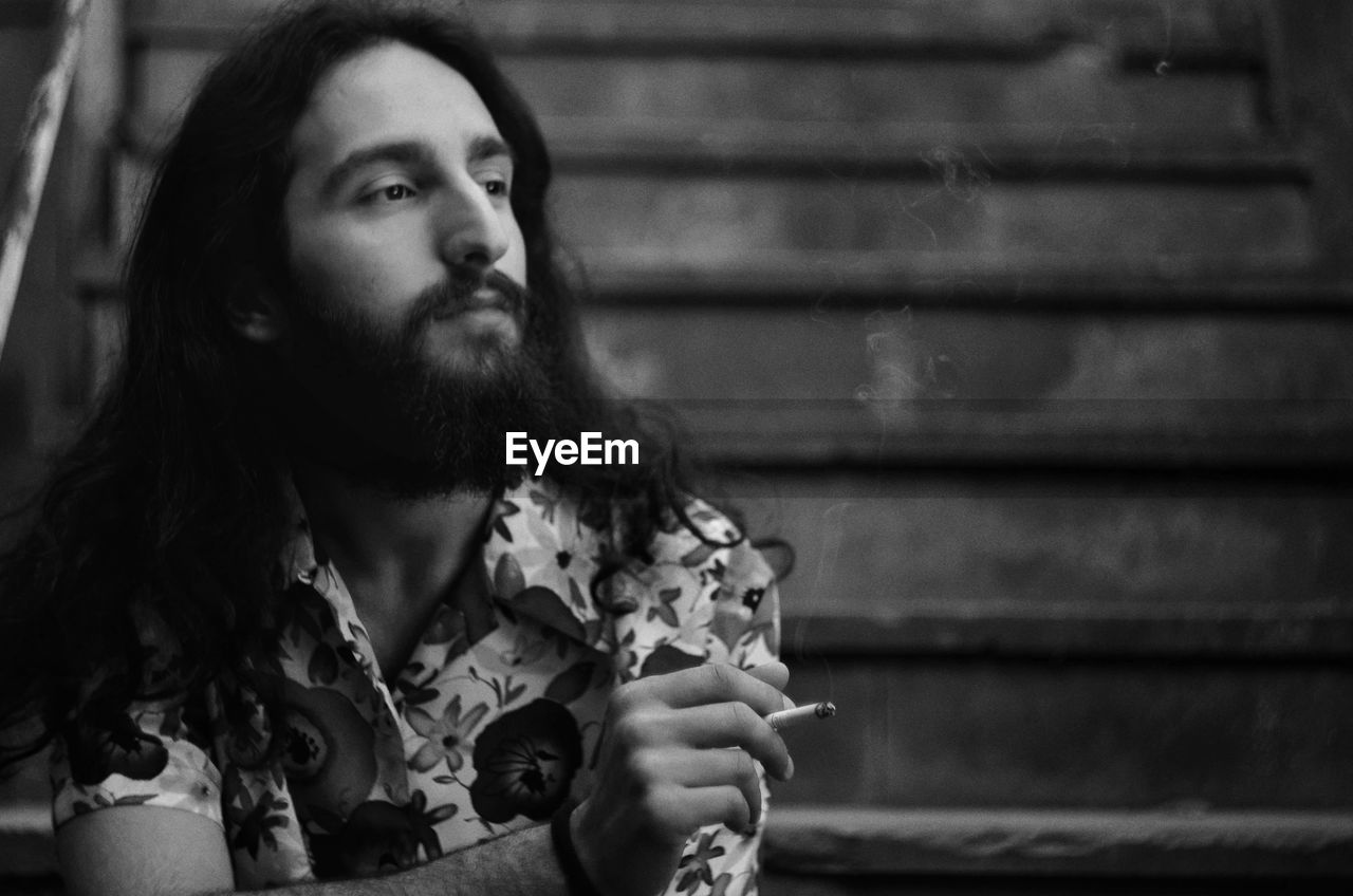 Thoughtful man smoking cigarette while sitting outdoors