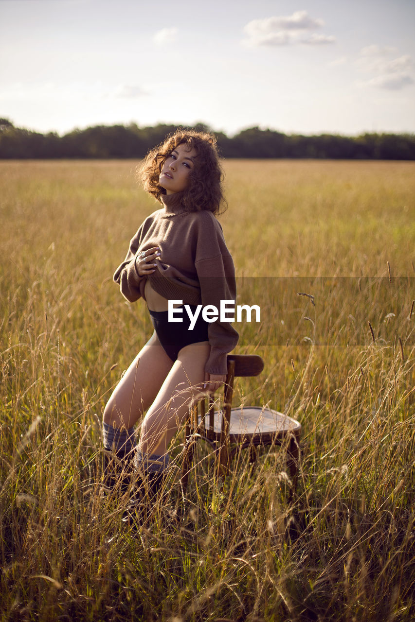 Fashion portrait of a curly-haired woman in a sweater and shorts sitting on a field with grass