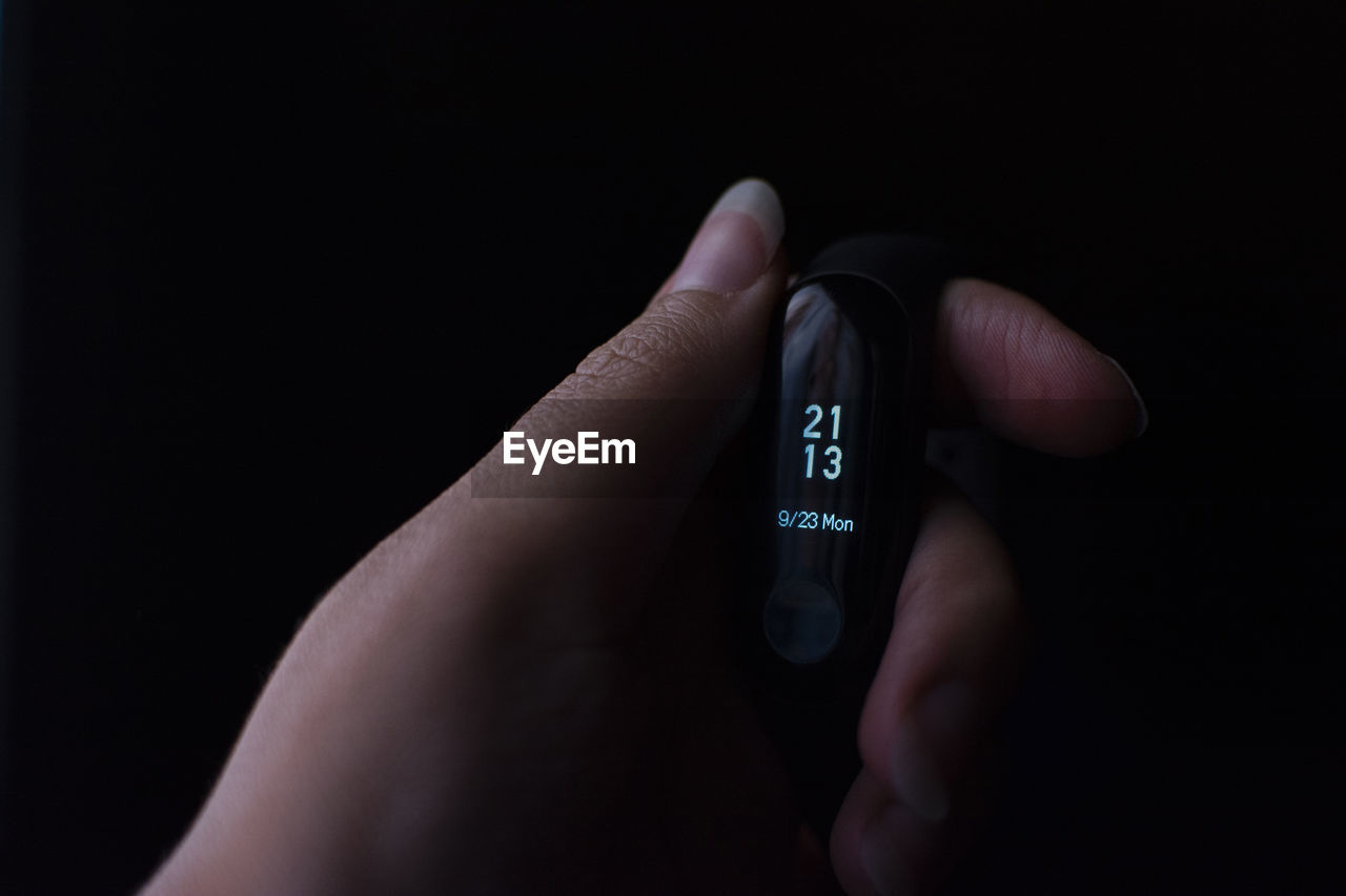 Close-up of hand holding smart watch against black background