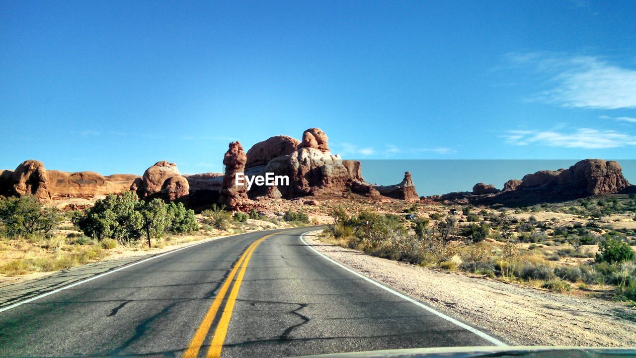 Empty country road leading towards rock formation against sky