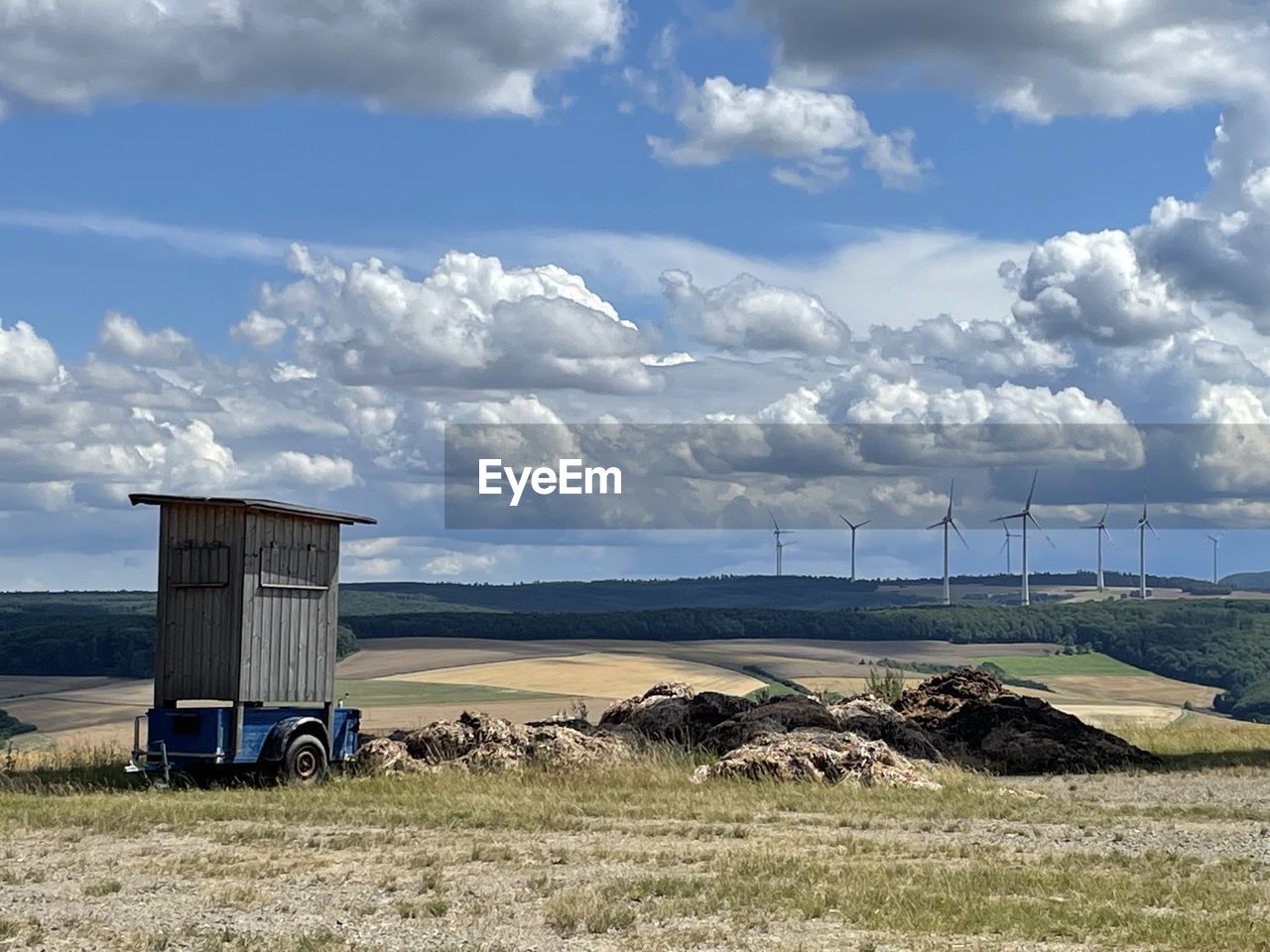 sky, rural area, cloud, environment, landscape, nature, field, land, prairie, power generation, scenics - nature, plain, grass, rural scene, day, horizon, built structure, no people, architecture, plant, transportation, windmill, sea, environmental conservation, beauty in nature, agriculture, outdoors, hill, non-urban scene, hut, farm, wind, coast, grassland, tranquility, renewable energy, vehicle, blue, tranquil scene, travel