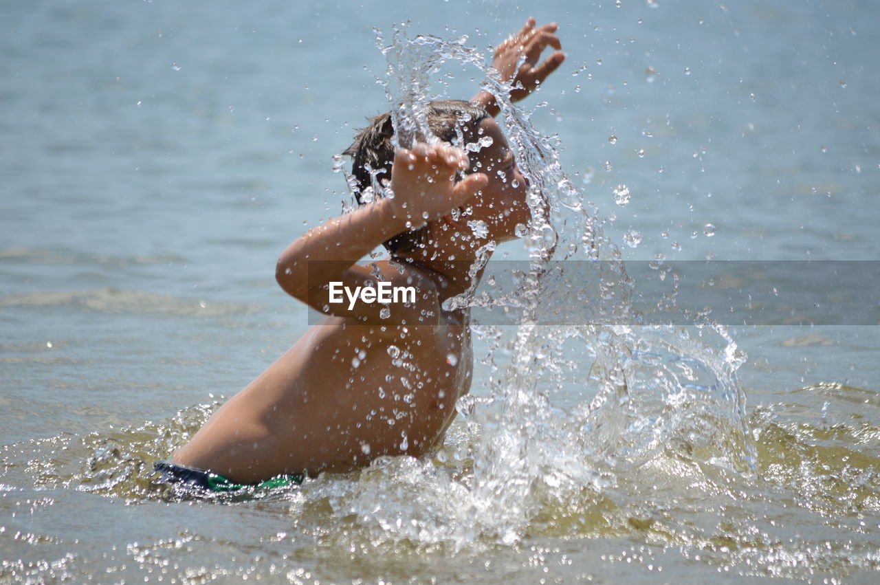 Side view of shirtless boy splashing water in lake