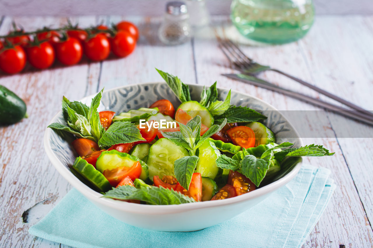 Fresh salad of cucumbers, cherry tomatoes and mint leaves in a bowl on the table