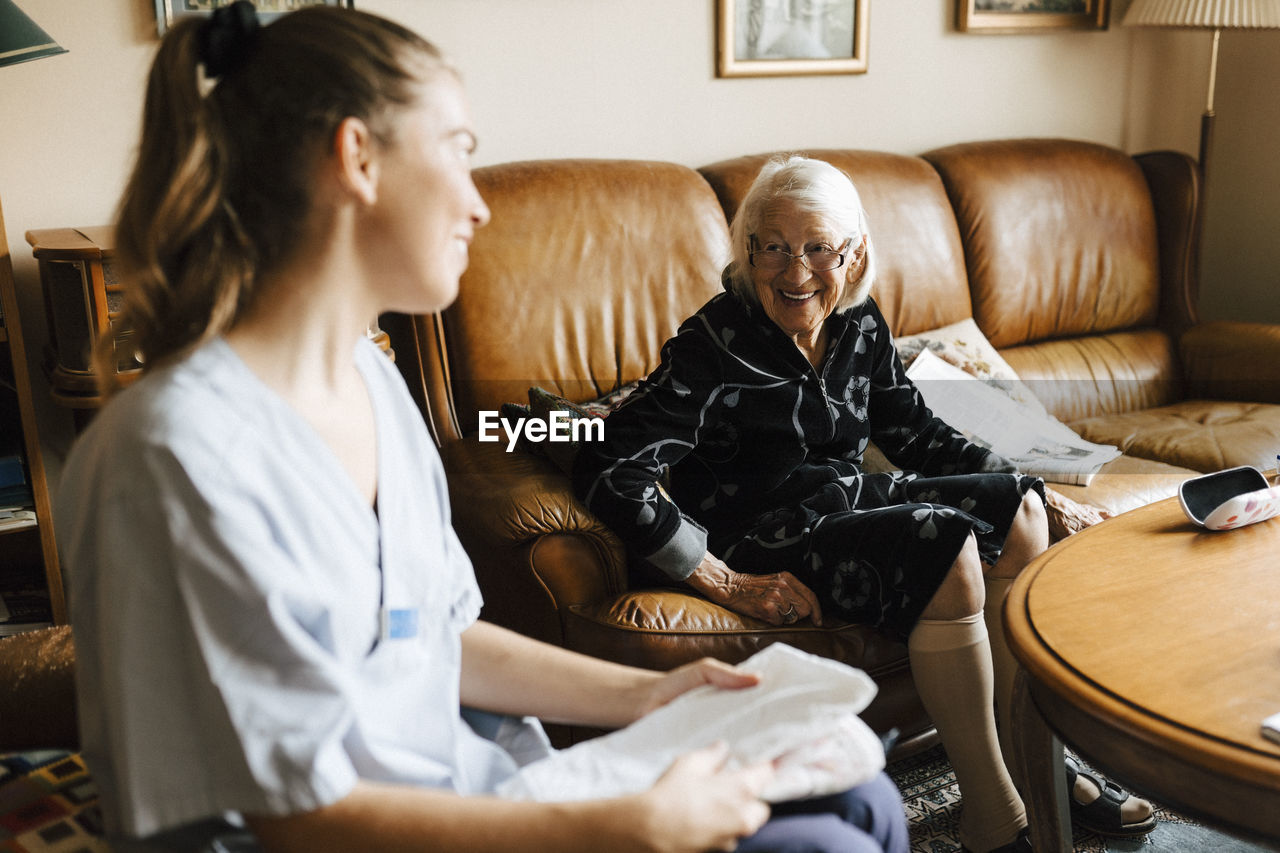 Smiling senior woman talking with female healthcare while sitting in living room at home
