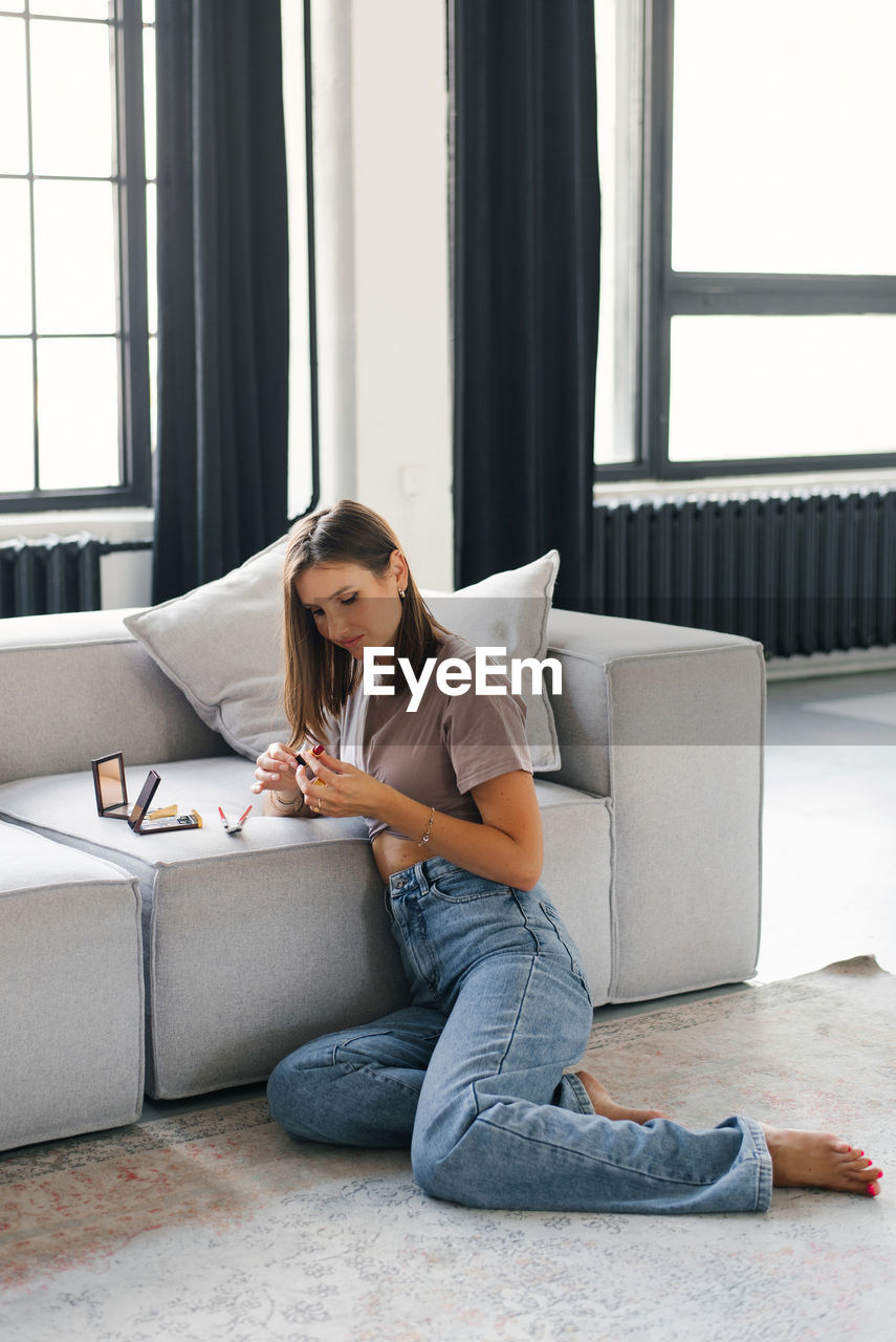 Young woman is sitting on the couch with makeup in front of her, about to do makeup person