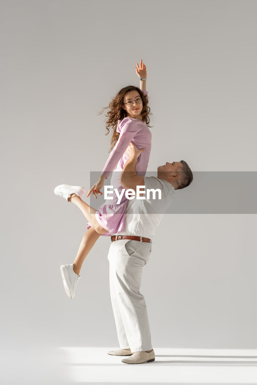 full length of young woman with arms raised standing against white background