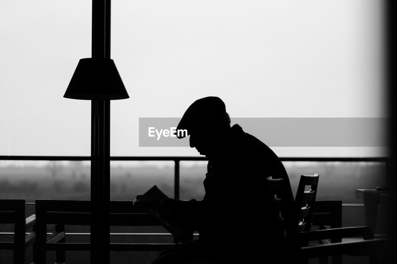 Side view of silhouette man sitting in restaurant against clear sky