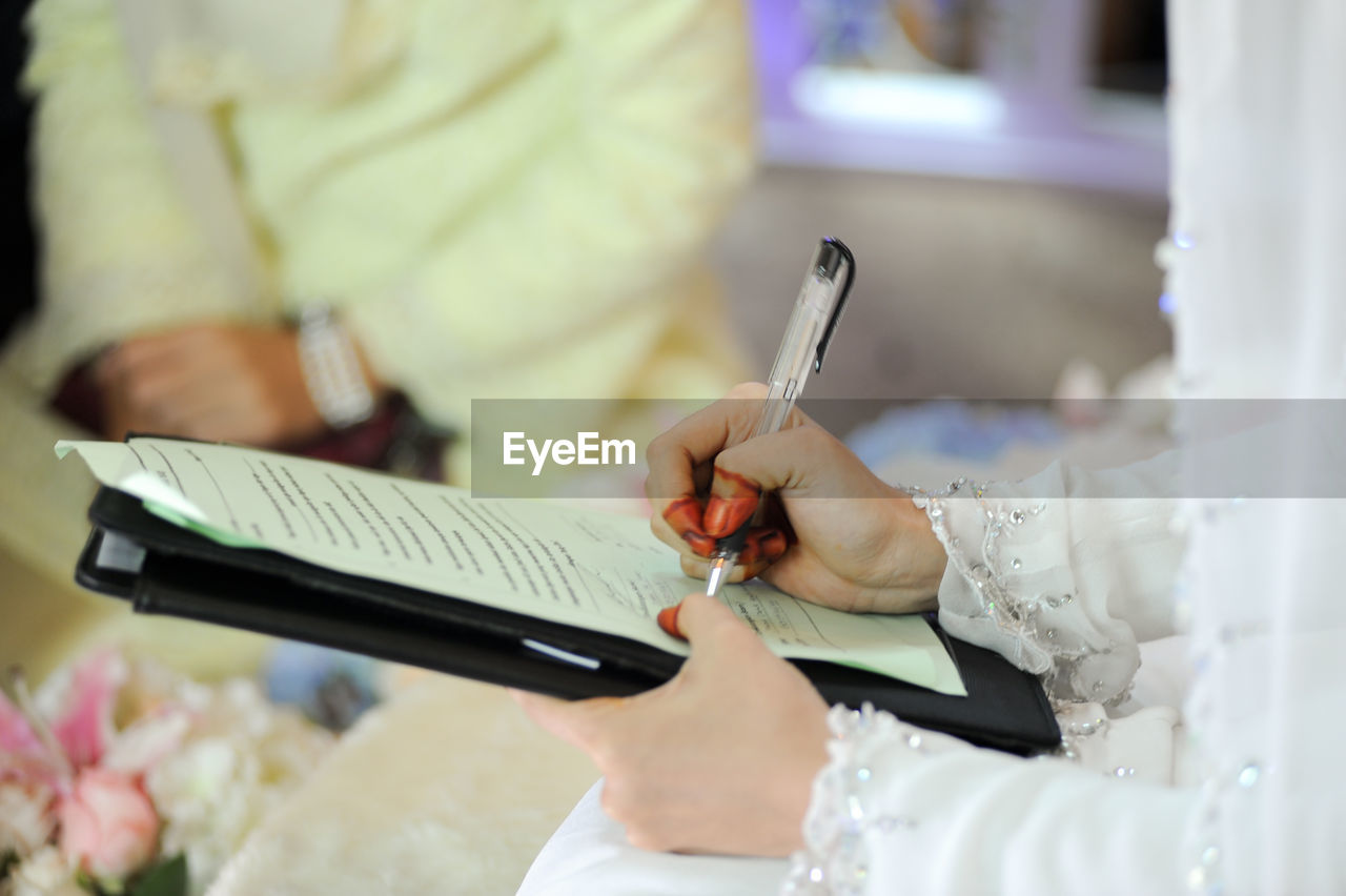 Midsection of bride signing marriage certificate