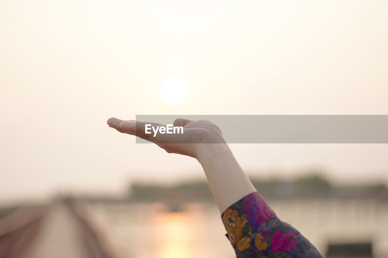 Cropped hand gesturing against sky during sunset