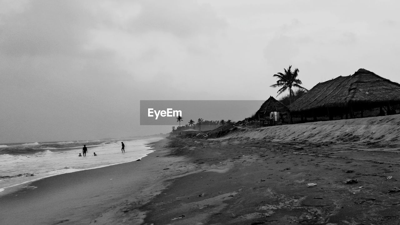 Thatched roof huts at sea shore against sky