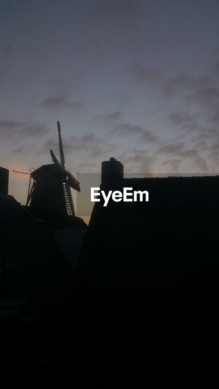 Low angle view of silhouette building and traditional windmill against sky