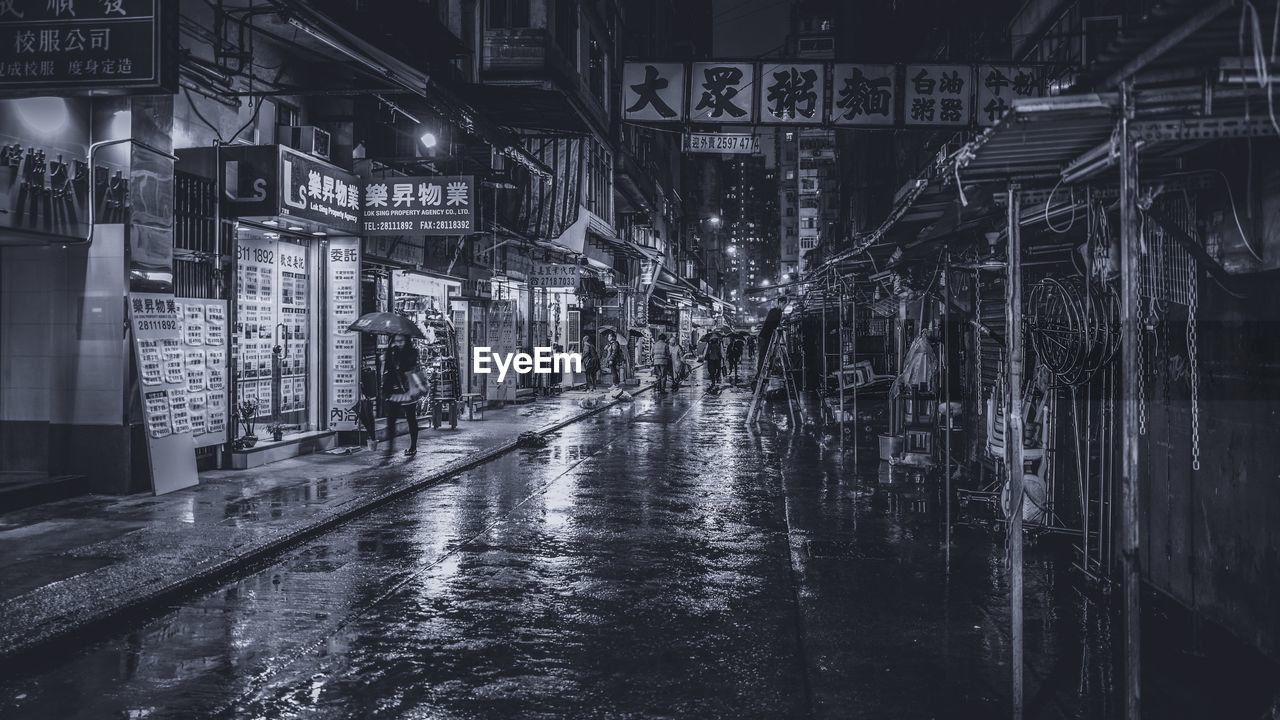 Woman with umbrella walking by wet street in city at night during rainy season
