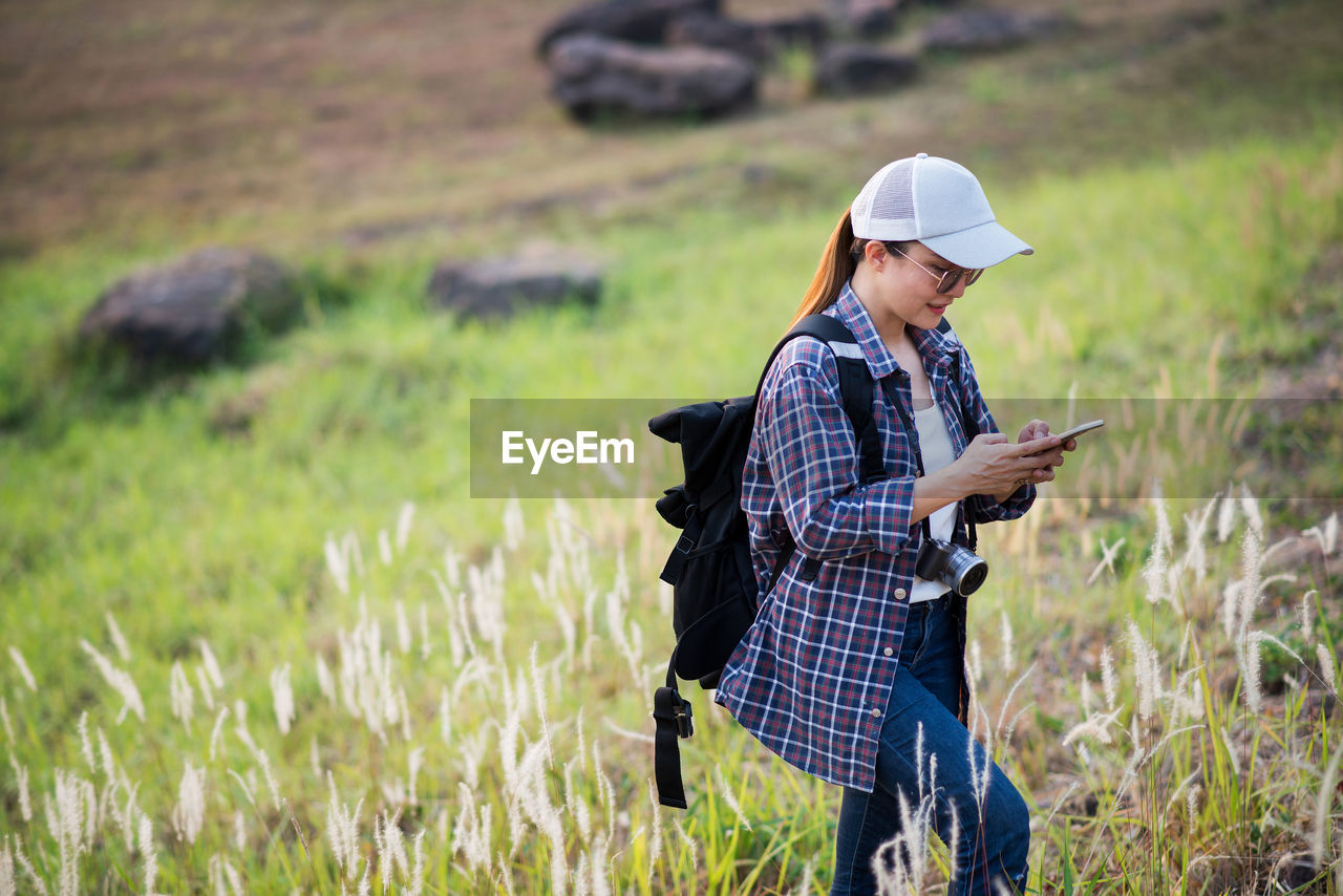 portrait of young woman using mobile phone while standing on field