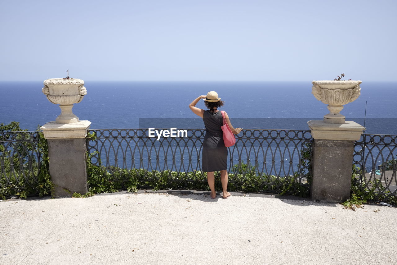 Rear view of woman standing by railing while looking at sea against sky