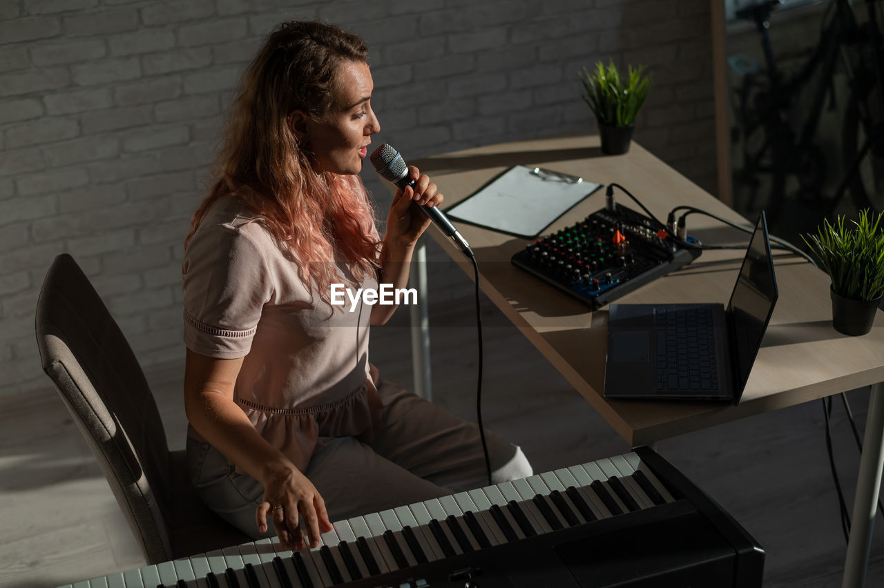 Young woman playing piano against wall at home