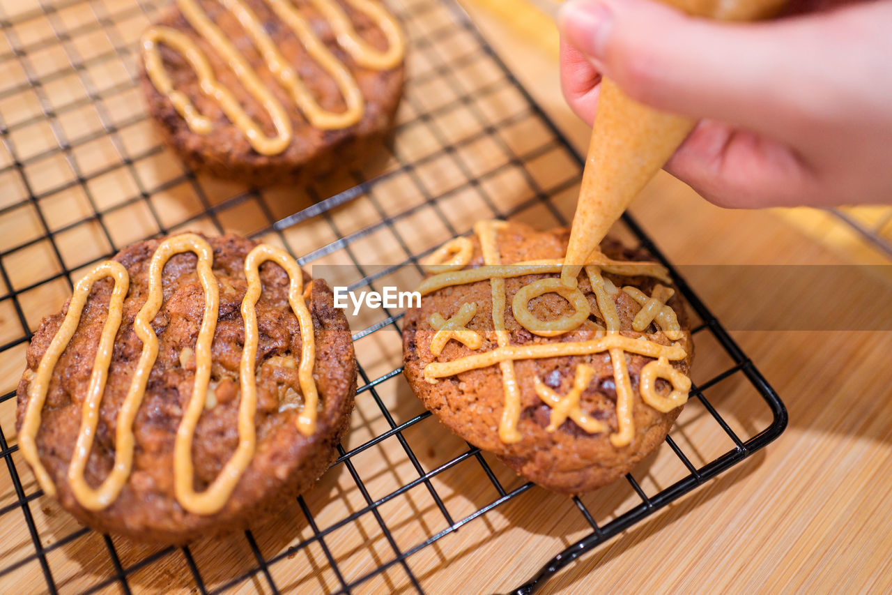 Cropped unrecognizable person hand in kitchen making chocolate chip biscuits with caramel sauce and male assistant