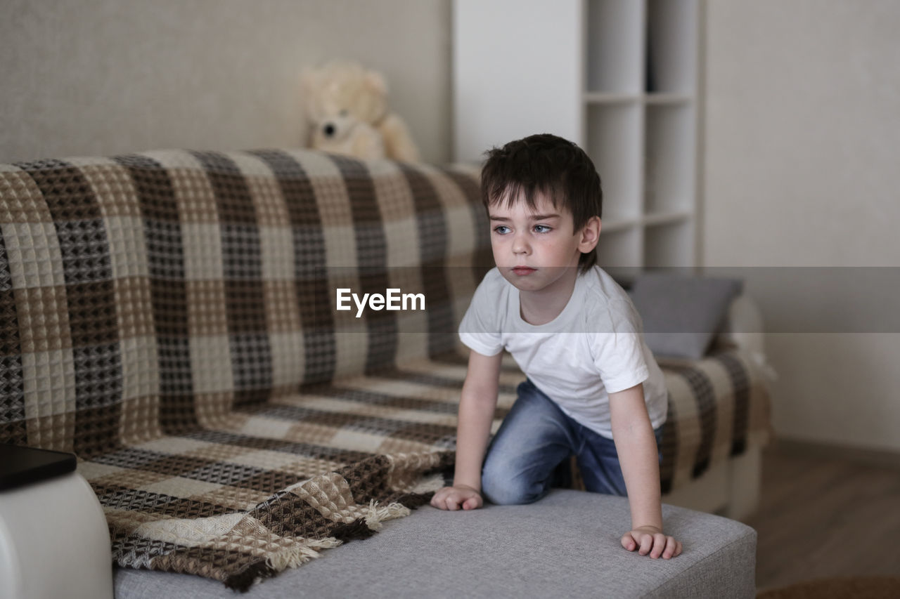 Boy toddler sad on the couch in the real room at home, lifestyles