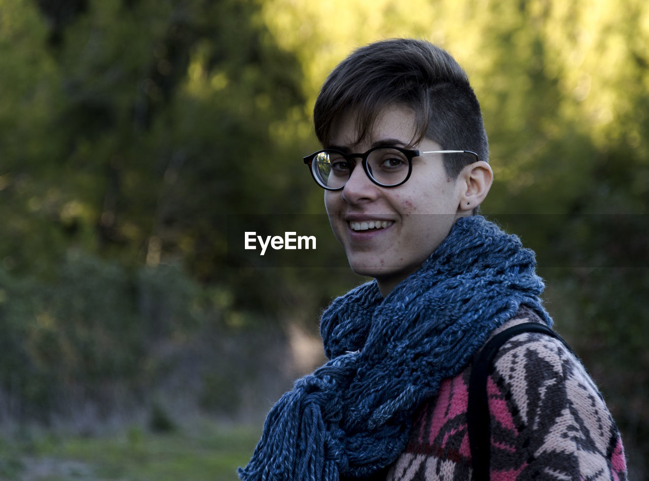 Side view portrait of smiling young woman wearing warm clothing and eyeglasses at park