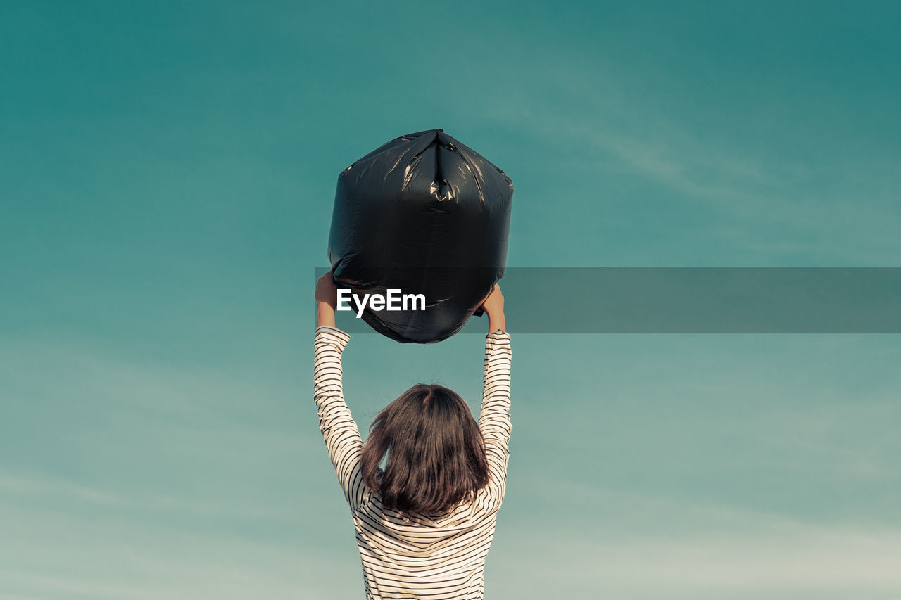 Rear view of girl holding garbage bag against sky