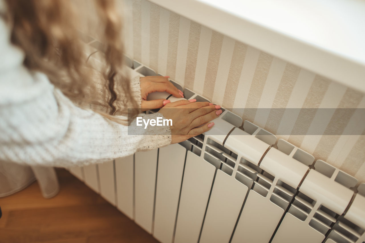 Hands of woman touching radiator at home