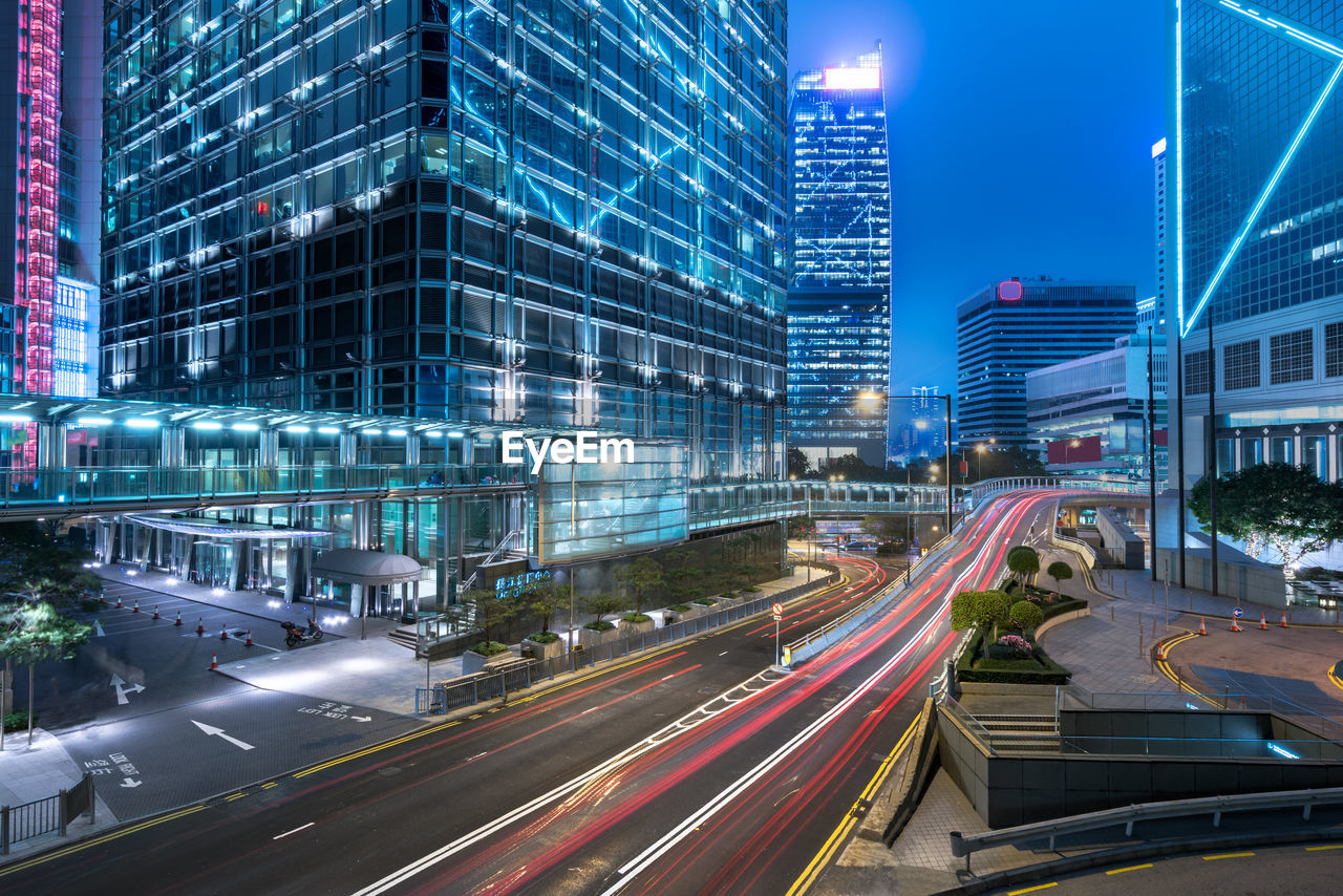 LIGHT TRAILS ON CITY STREET BY BUILDINGS AT NIGHT