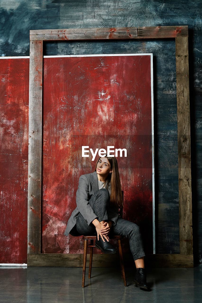 Full length of woman sitting on chair against wall