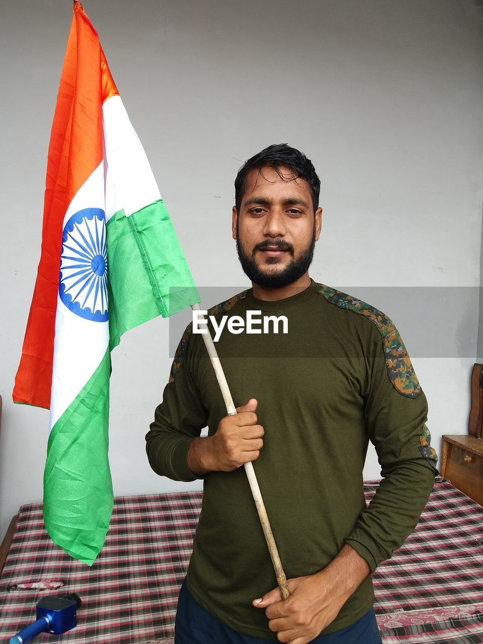 Portrait of young man holding indian flag standing against wall