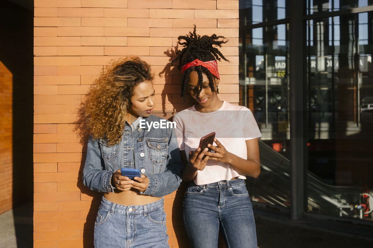 Young woman showing mobile phone to friend on sunny day