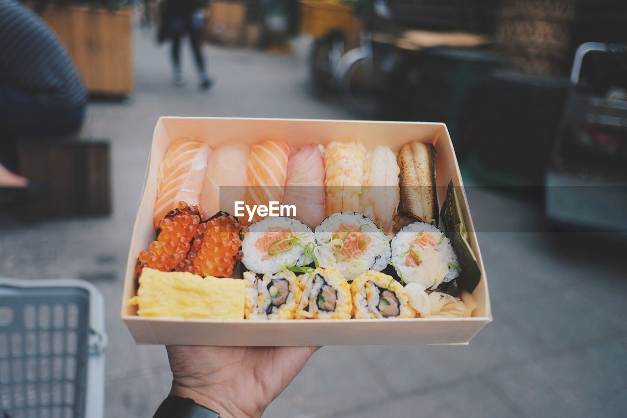 Cropped hand of man holding sushi in container