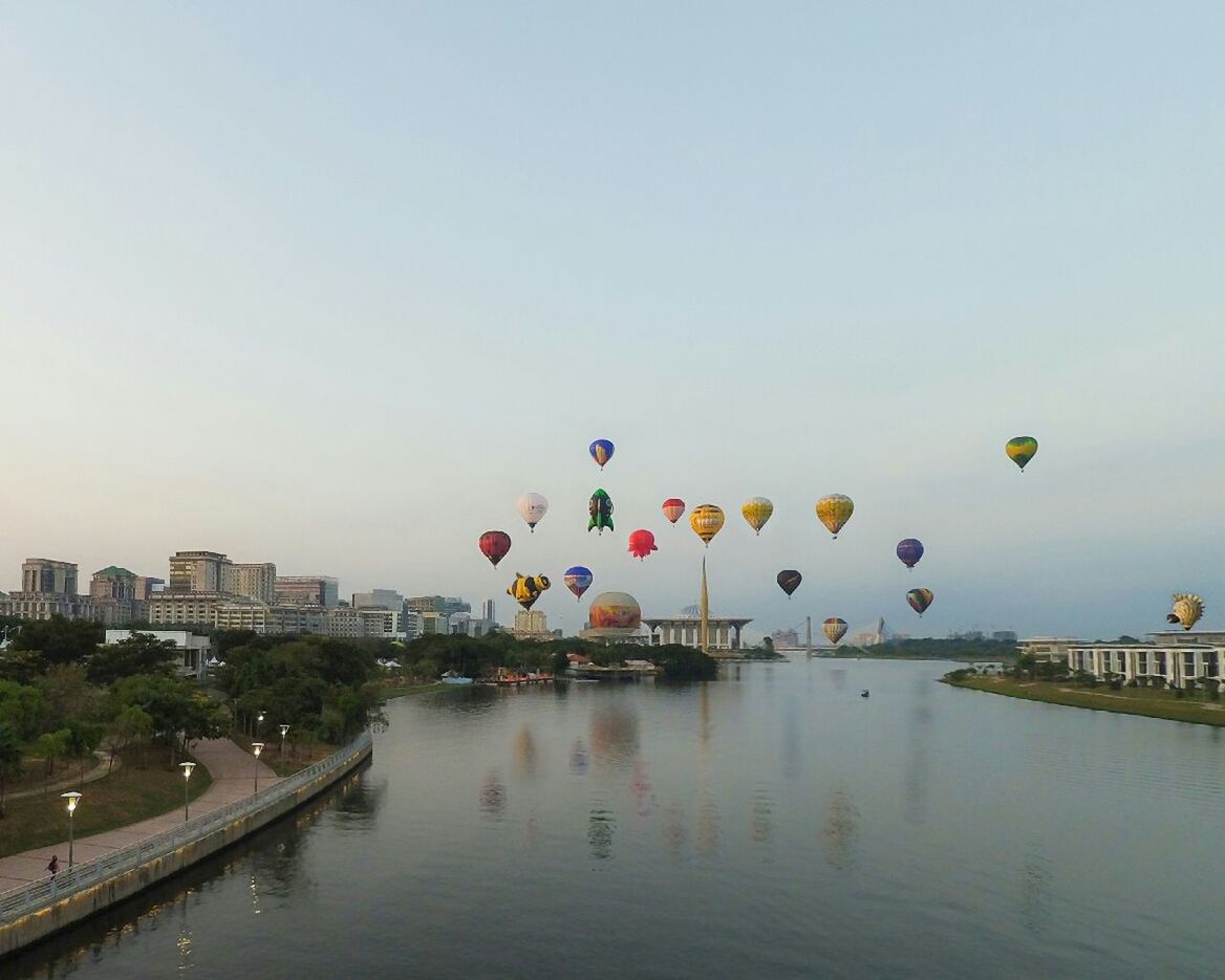 Colorful hot air balloons flying over putrajaya lake against sky