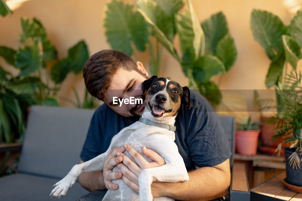 MAN AND DOG SITTING ON PLANT IN ROOM