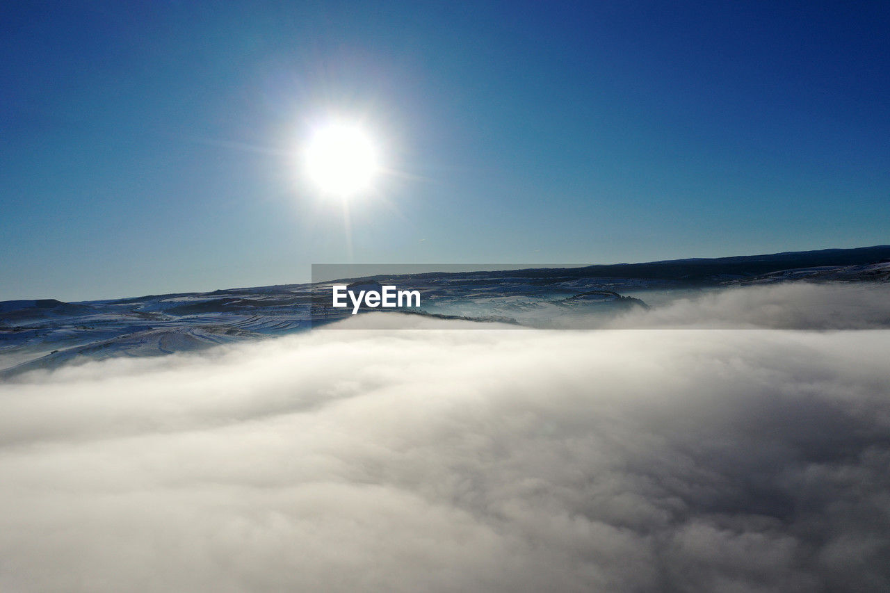 sky, cloud, horizon, environment, nature, sunlight, beauty in nature, sun, blue, scenics - nature, cloudscape, sunbeam, no people, mountain, clear sky, outdoors, copy space, light, idyllic, landscape, wave, atmosphere, travel, snow, tranquility, lens flare, sea, bright, day, high up, sunny, aerial view, white, awe, light - natural phenomenon, tranquil scene