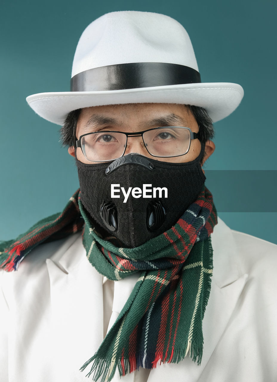 Portrait of man wearing mask and hat against colored background