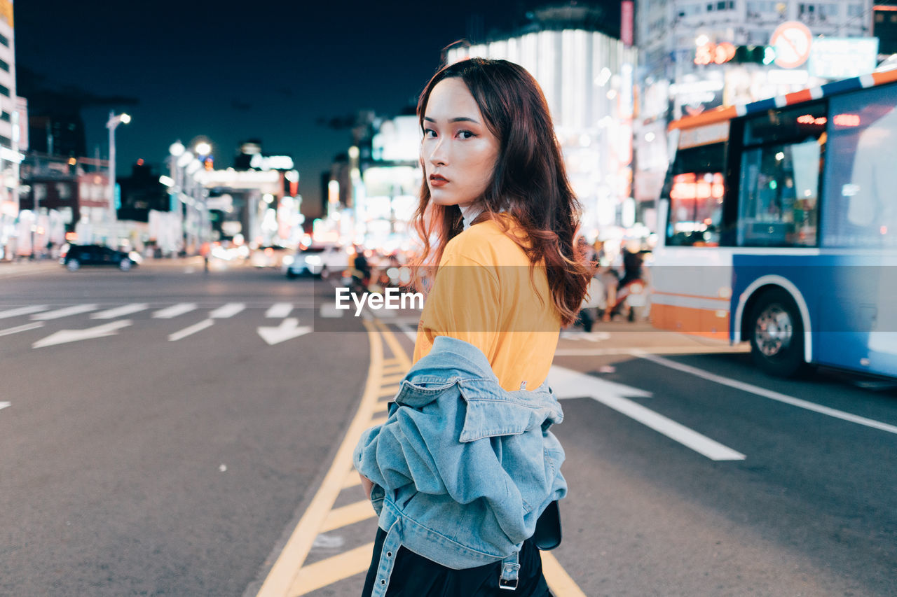 YOUNG WOMAN STANDING BY ROAD IN CITY