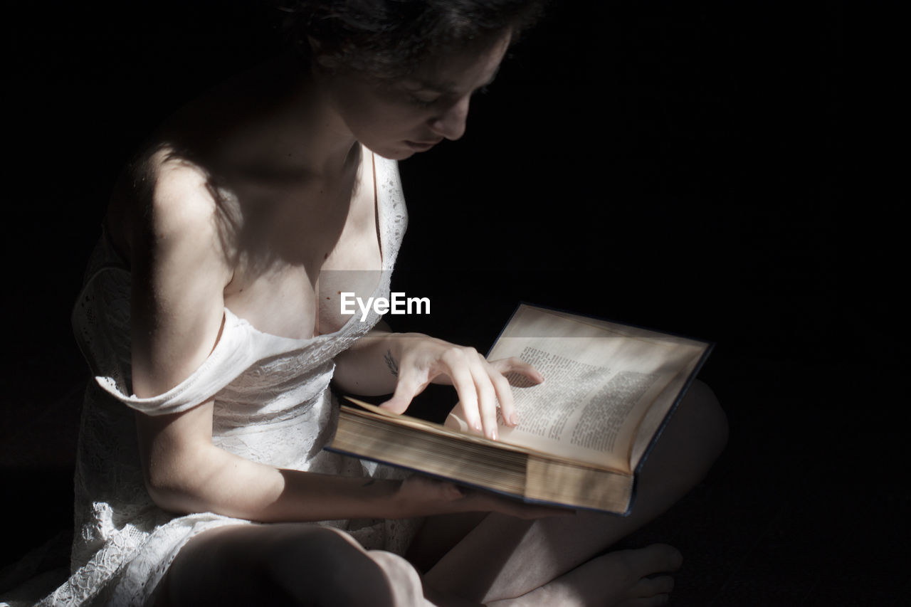 Woman reading book while sitting over black background