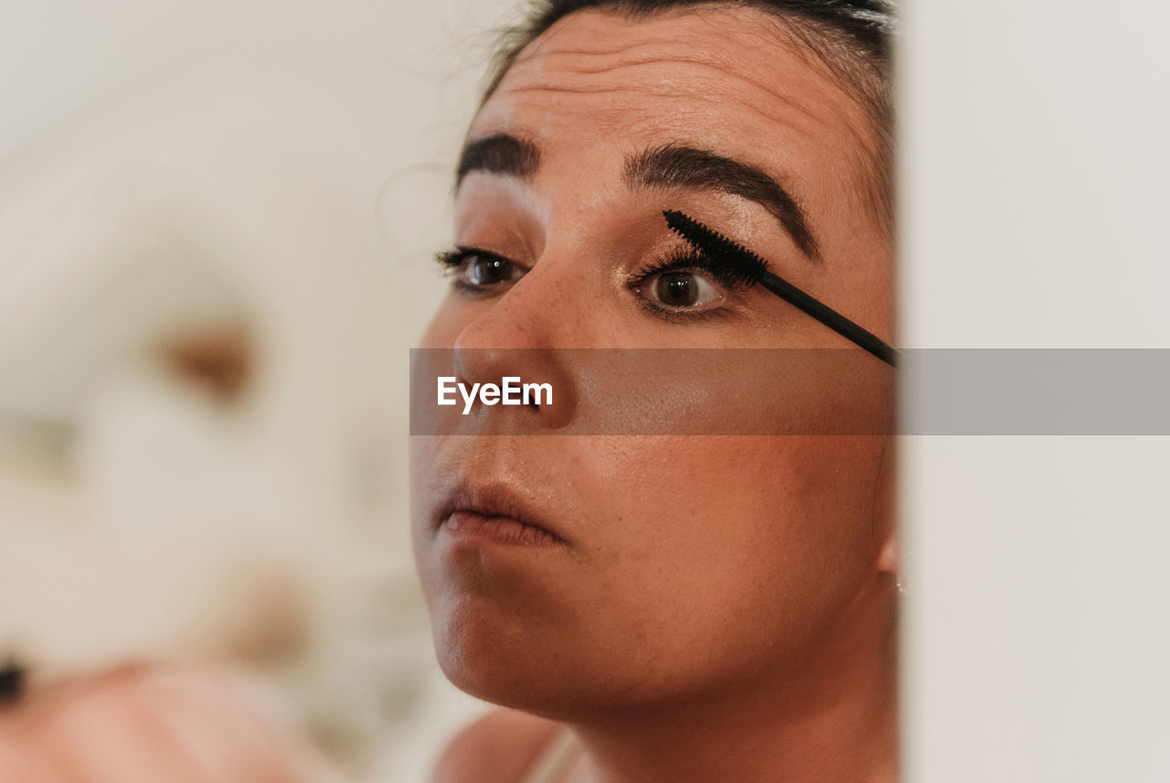 Mirror photo of beautiful young woman putting on makeup