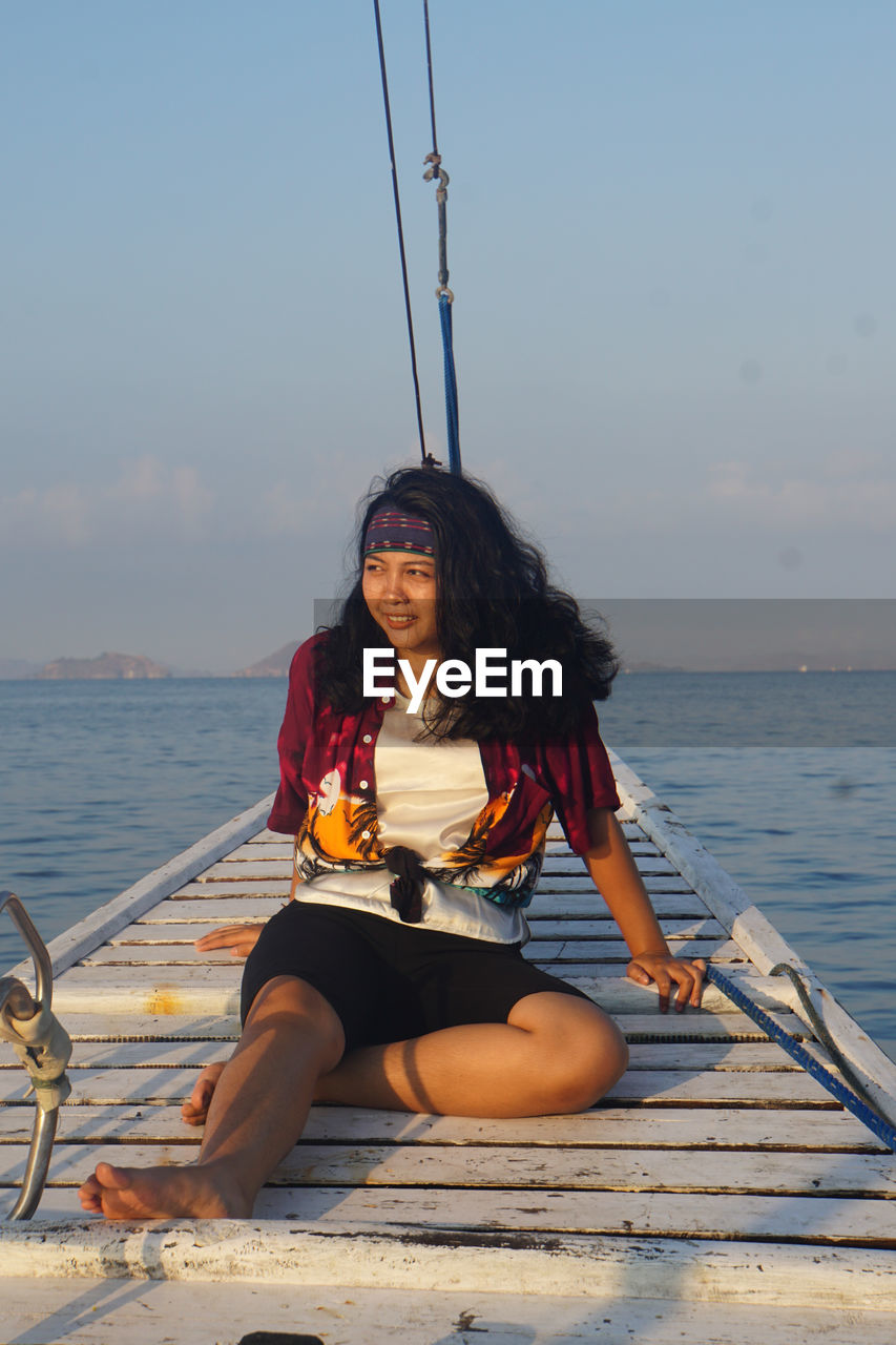 WOMAN SITTING IN BOAT AGAINST SEA