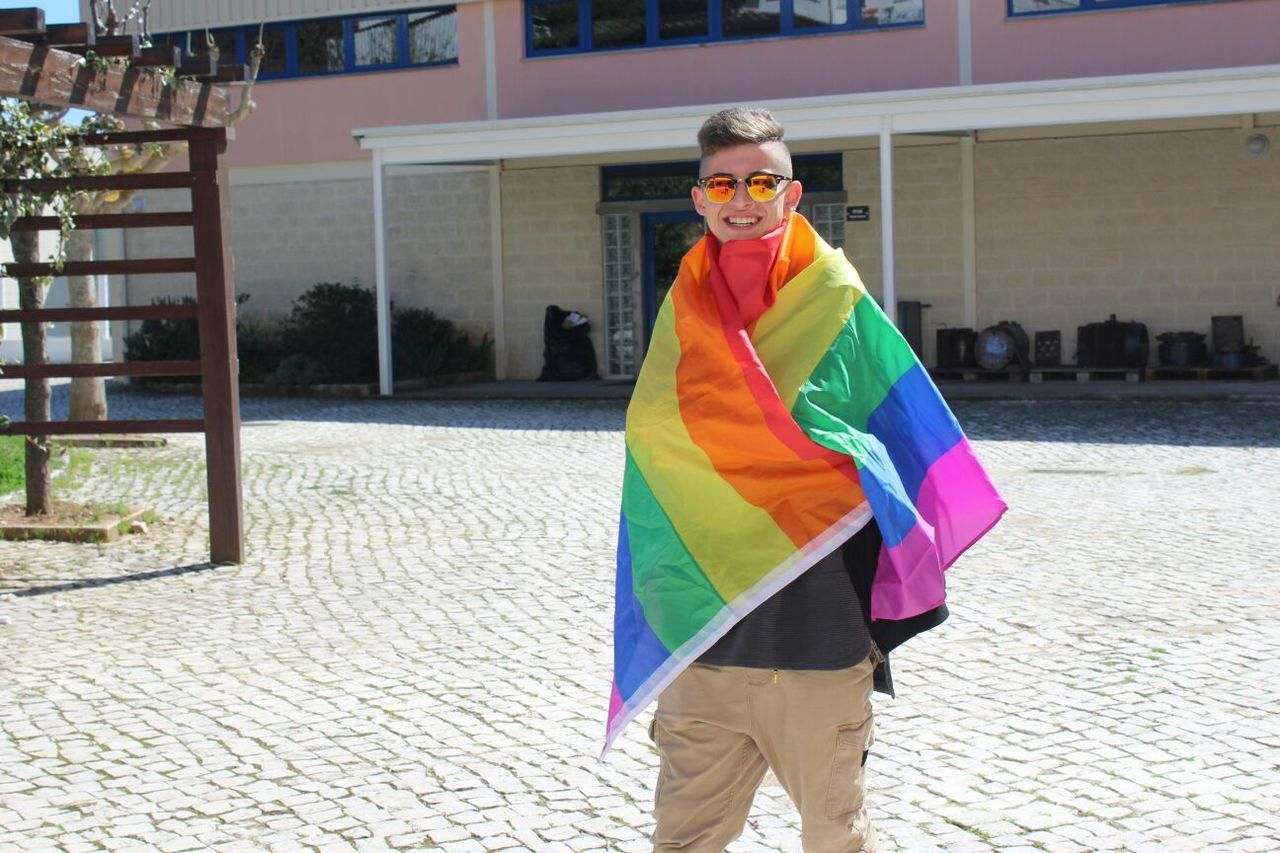 Happy gay man wrapped in rainbow flag on street