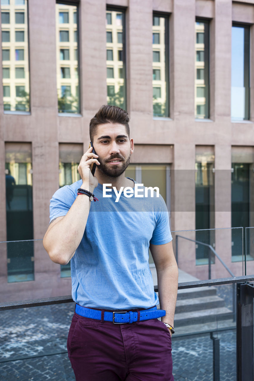 Young businessman talking on phone while standing against building in city