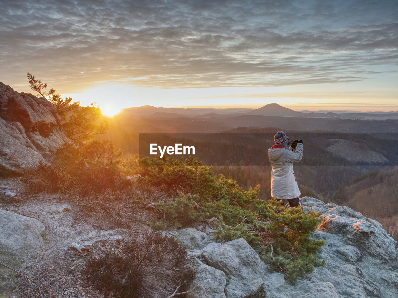 Photograper with hand on camera and tripod. woman climbed up on exposed rock for fall photos 