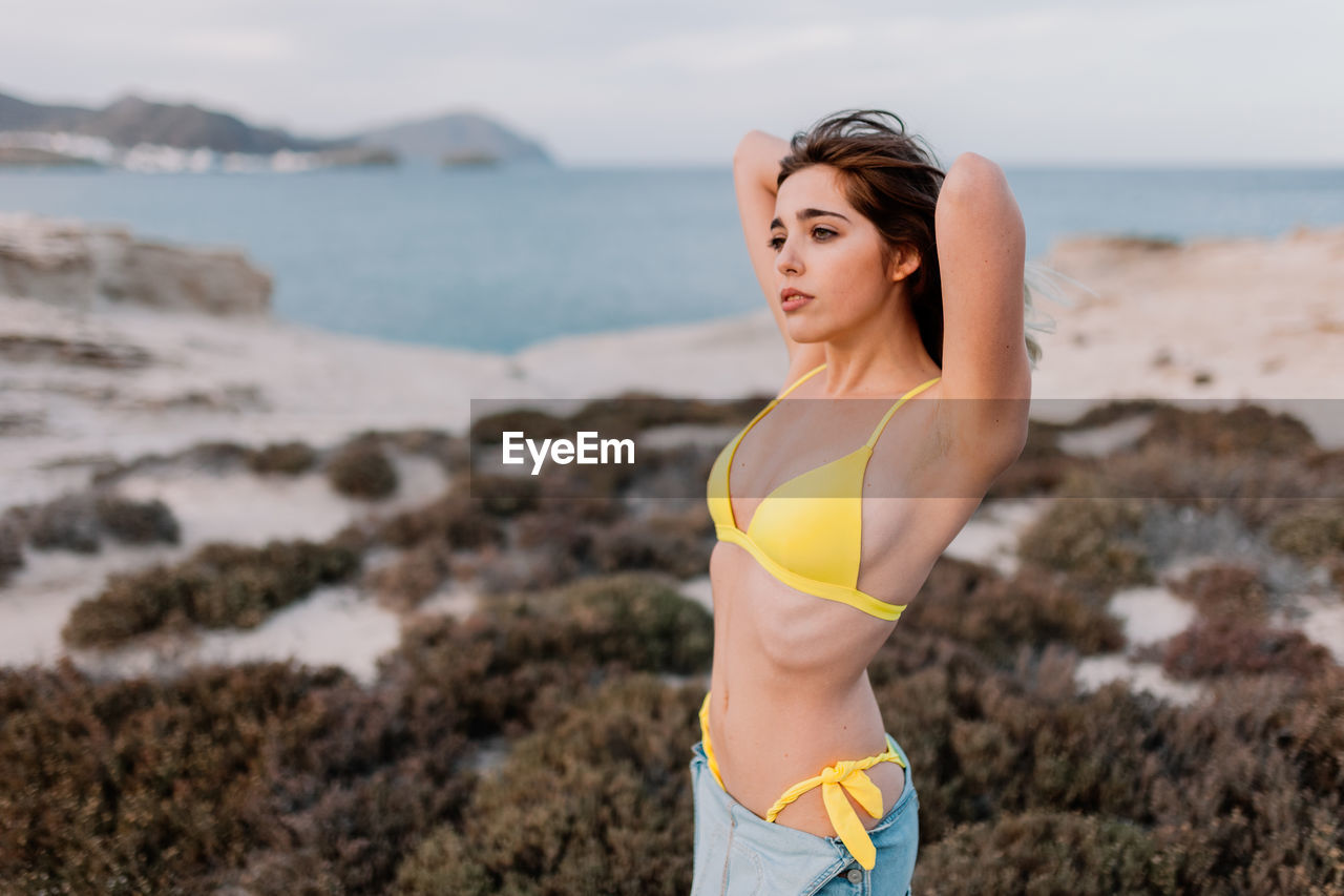 Carefree young woman with hand in hair standing on shore at beach