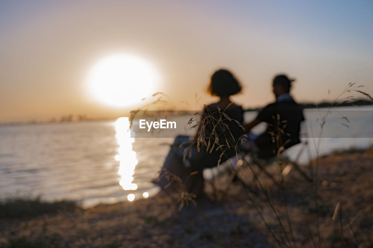 Rear view of people sitting at beach during sunset