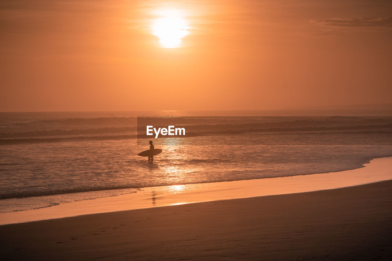 Surfer standing in sea during sunset
