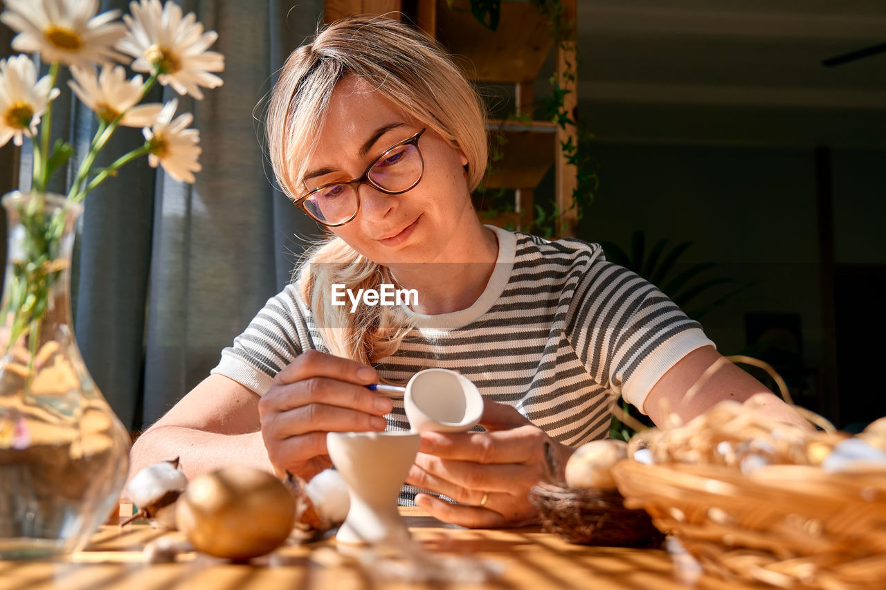 Blond woman preparing easter decoration at home, painting colorful easter eggs and coloring egg cups